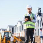 professional surveyor working with a digital tablet and total station, managing land measurements at a residential development construction site
